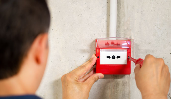 a person is  hands installing a red fire alarm pull station on a concrete wall