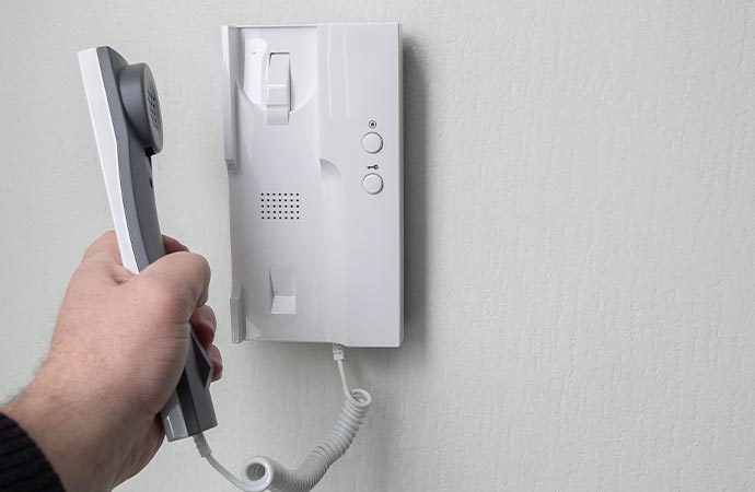 a person is holding a white telephone handset connected to an audio intercom system mounted on a wall